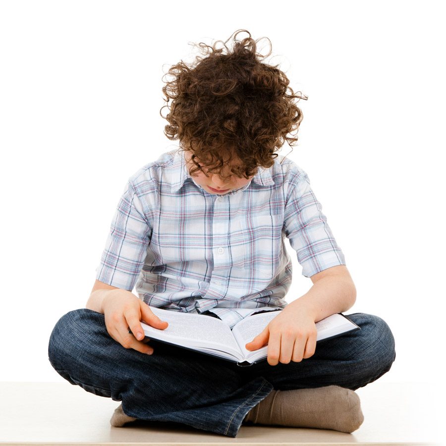 Curly-haired boy sitting cross-legged on the floor reading an open book