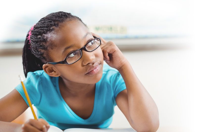 A thoughtful girl in glasses rests her head on her hand while writing with a pencil.