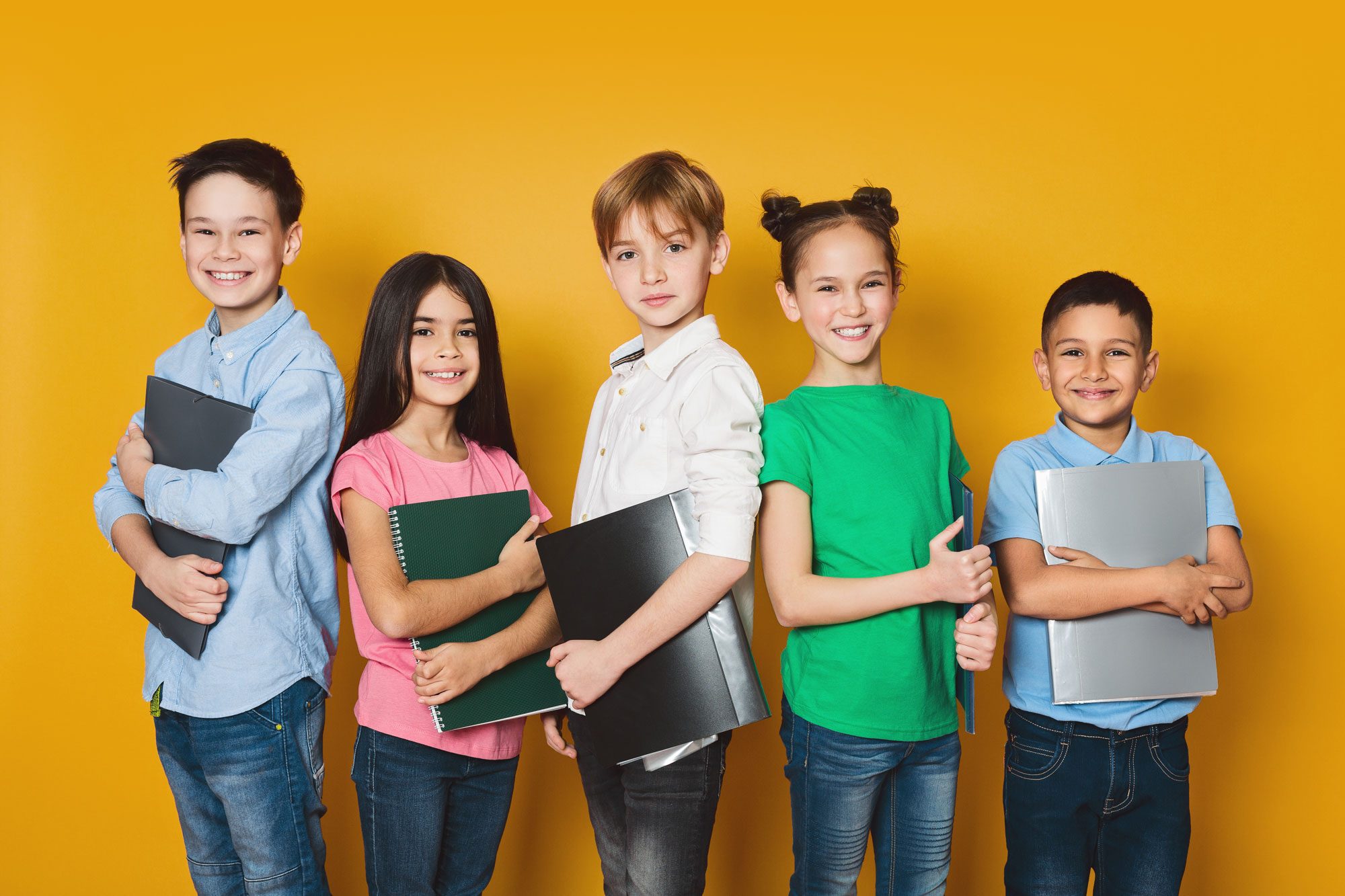Five smiling students holding binders and notebooks against a gold background.
