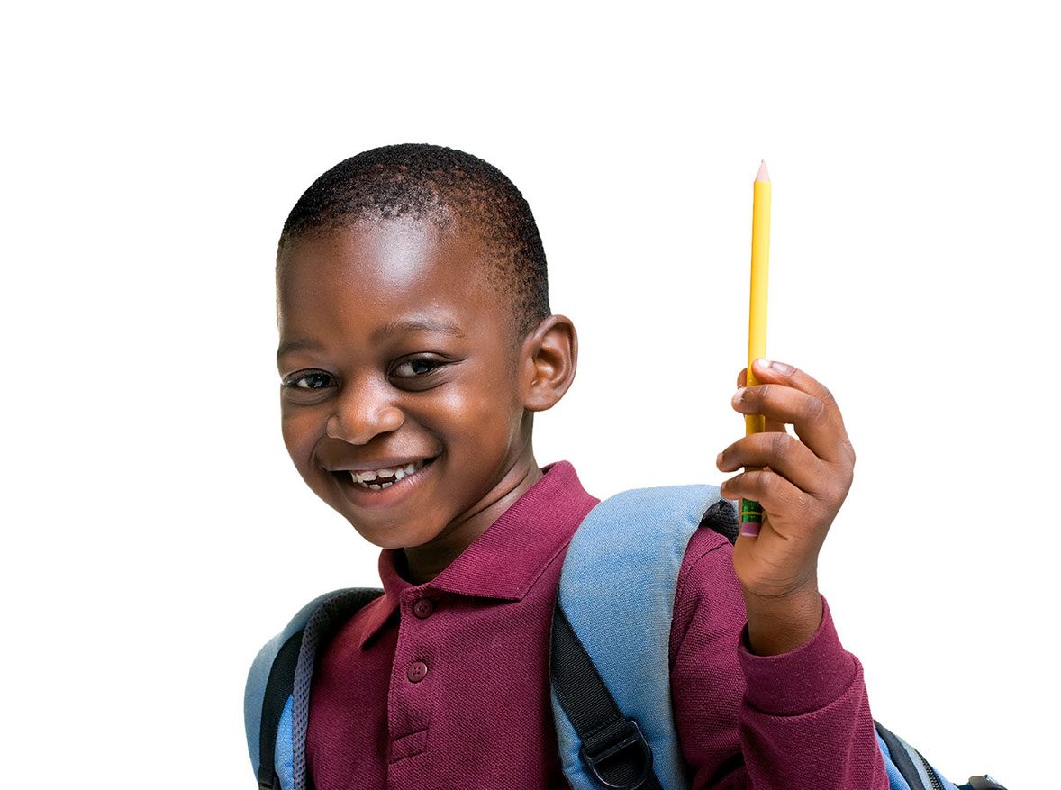 A smiling boy wearing a backpack holds up a yellow pencil.