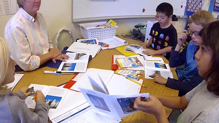 A teacher and students gathered around a table covered with books and papers